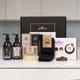 Pamper Treat Box For Him. A gift set displayed on a white countertop, featuring two pump bottles of liquid body wash and body lotion, soap packaged in a decorative box, a pair of black socks, and a box of assorted chocolates. The items are arranged around a sleek black gift box labeled "giftsdirect." Pamper Treat Box For Him. A gift set displayed on a white countertop, featuring two pump bottles of liquid body wash and body lotion, soap packaged in a decorative box, a pair of black socks, and a box of assorted chocolates. The items are arranged around a sleek black gift box labeled "giftsdirect."